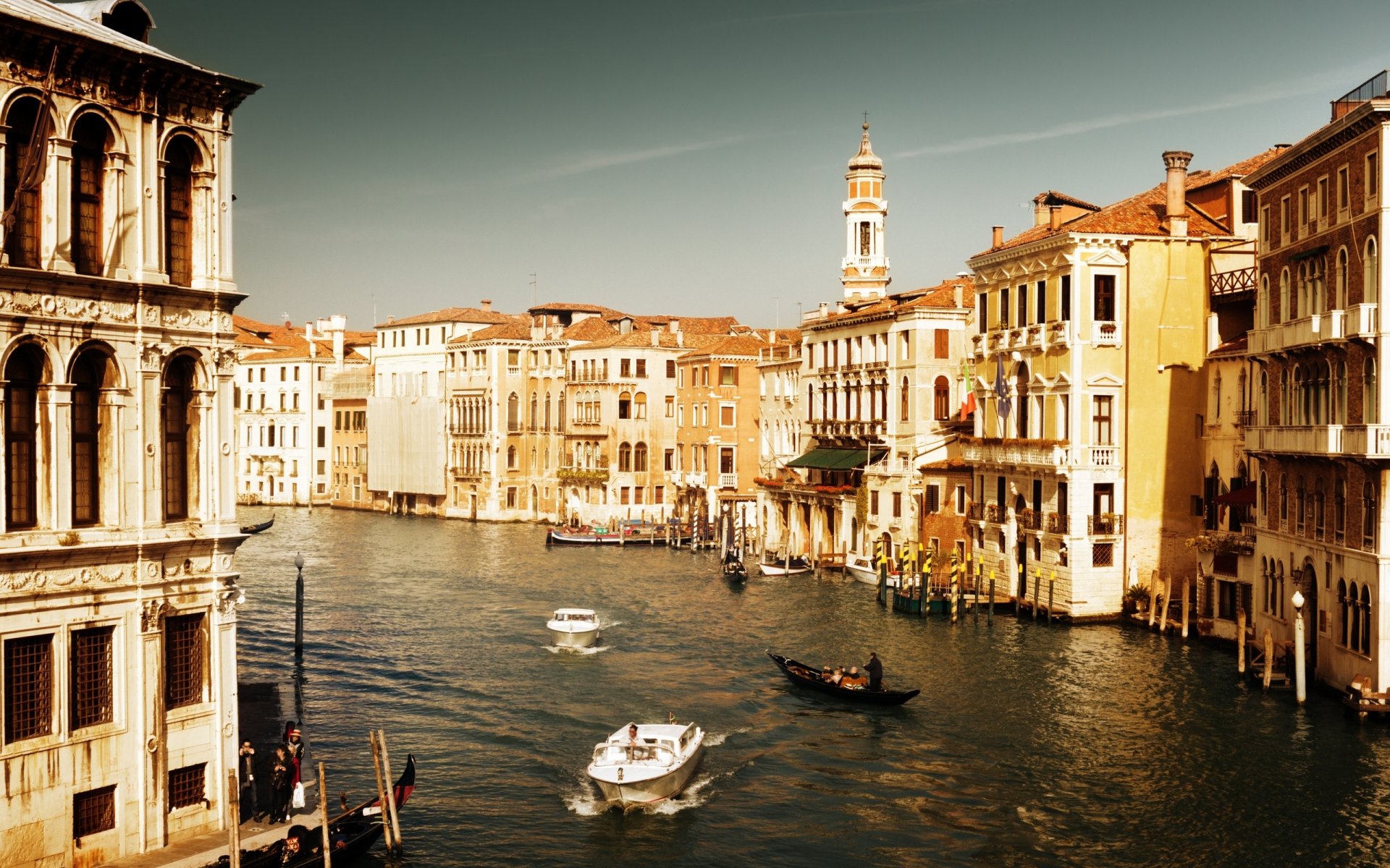 A serene view of Venice, showcasing its iconic architecture along the canal with boats gently traversing the water, featured as a high-definition desktop wallpaper.