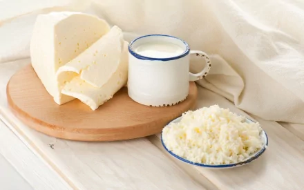 HD desktop wallpaper featuring cheese on a wooden board, a white mug filled with milk, and a plate of ricotta cheese on a light-colored surface with a soft fabric background.