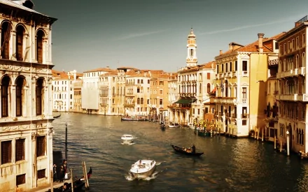 A serene view of Venice, showcasing its iconic architecture along the canal with boats gently traversing the water, featured as a high-definition desktop wallpaper.