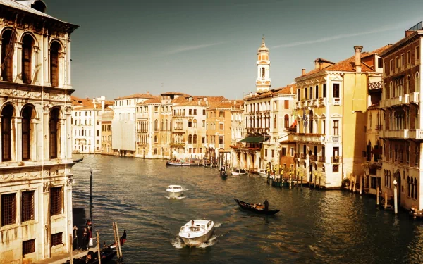 A serene view of Venice, showcasing its iconic architecture along the canal with boats gently traversing the water, featured as a high-definition desktop wallpaper.