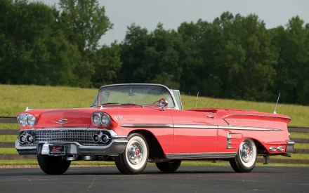 A striking Chevrolet Impala convertible from 1958 stands against a lush green backdrop, showcased as a vibrant HD desktop wallpaper.
