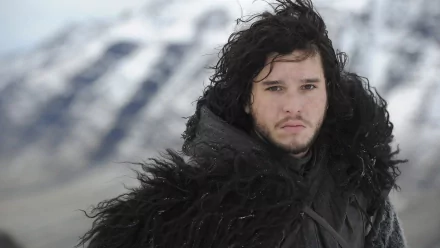 HD desktop wallpaper featuring Kit Harington as Jon Snow from the TV show Game of Thrones. He stands in front of a snowy mountainous backdrop, dressed in dark, heavy furs.