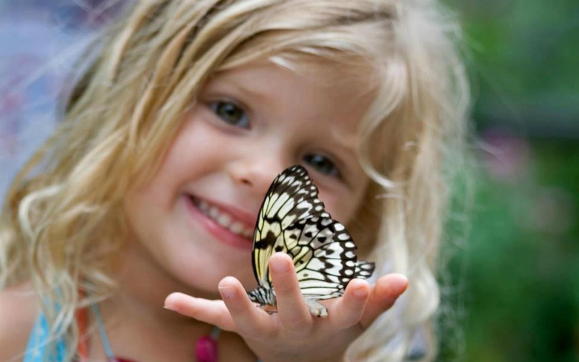 A smiling child holds a delicate butterfly on her outstretched hand, captured in vibrant detail, making a lovely HD desktop wallpaper and background.