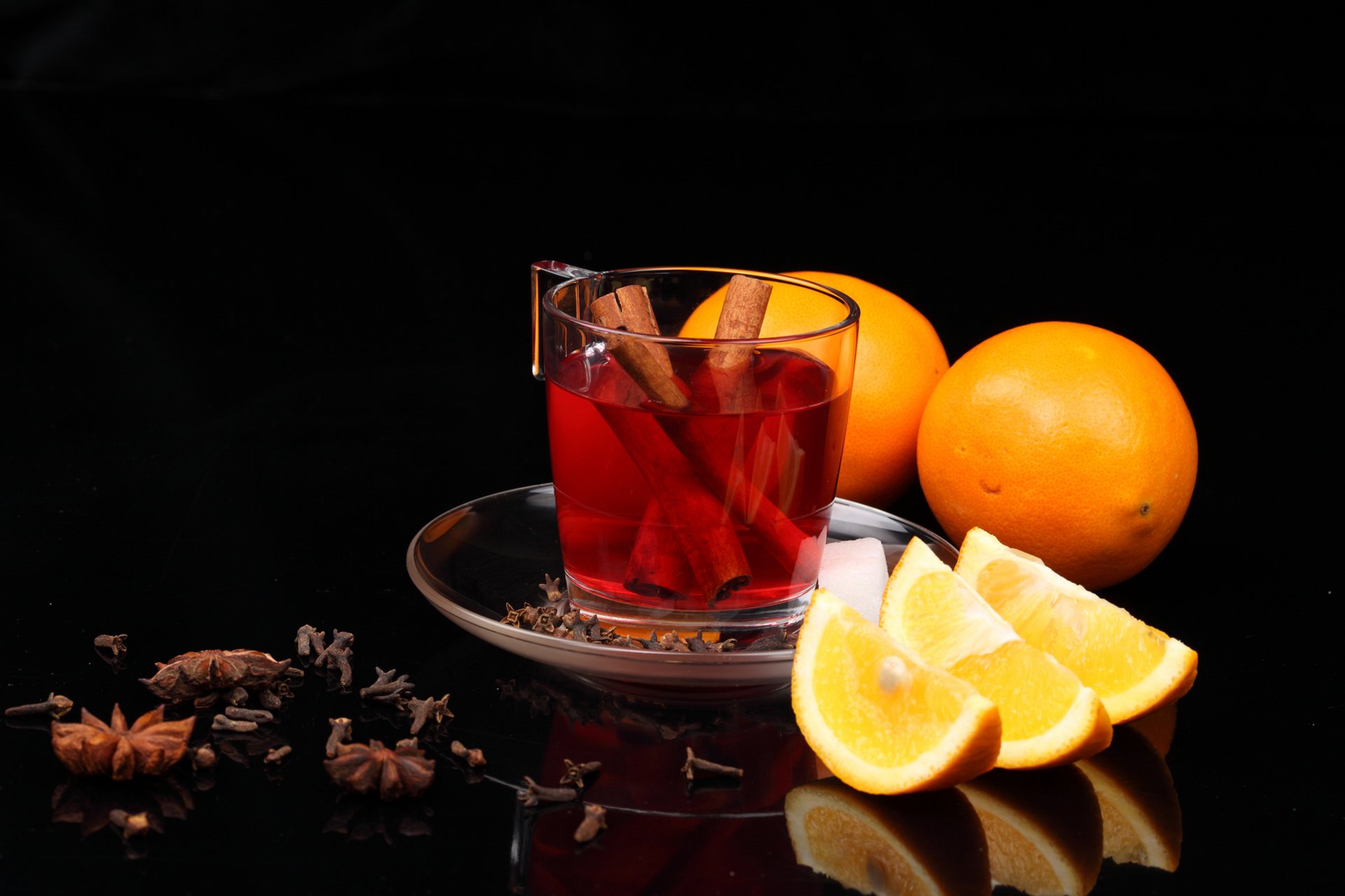 4K Ultra HD desktop wallpaper featuring a glass of spiced tea with cinnamon sticks, sliced oranges, and whole oranges on a reflective black surface, styled as food and tea.