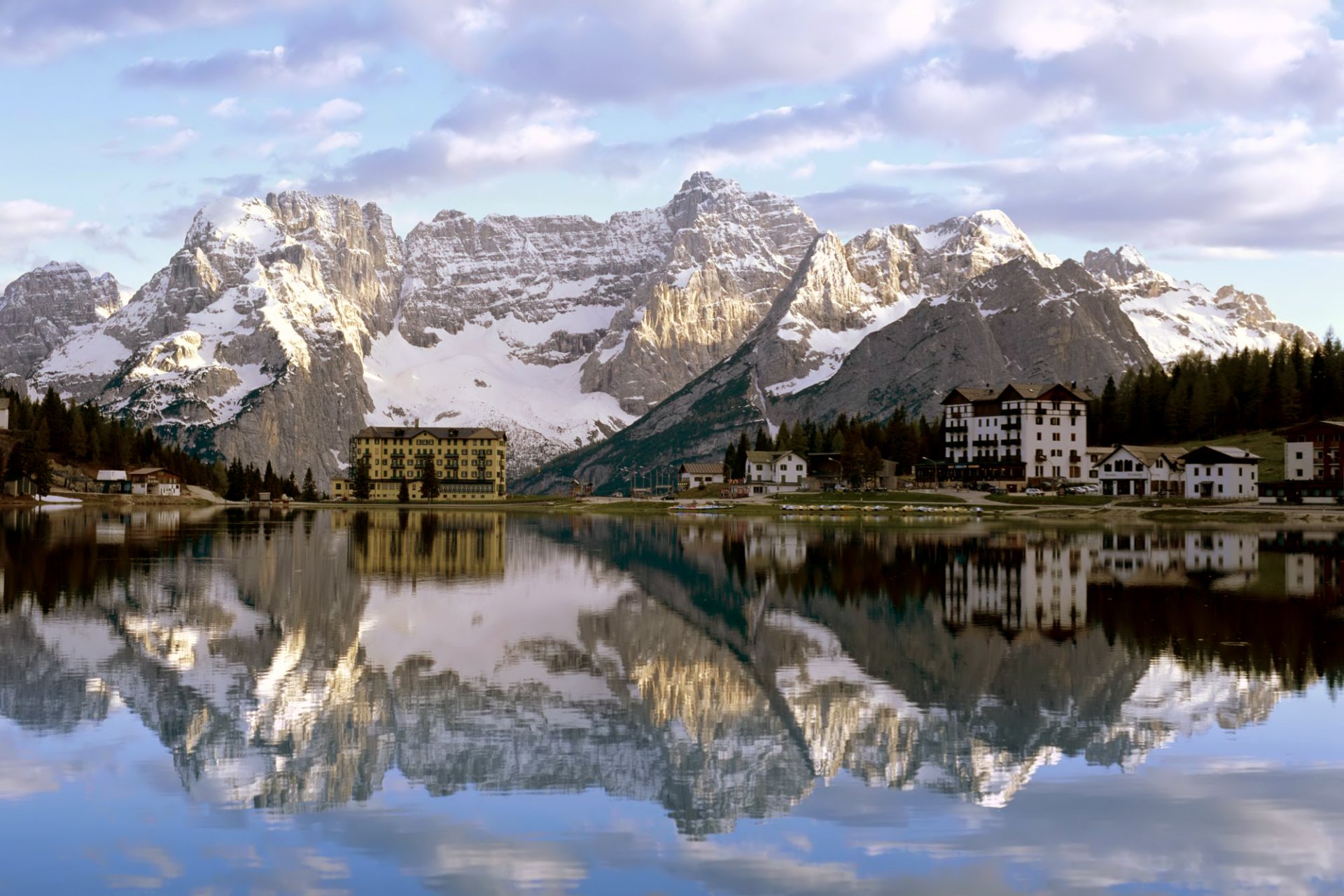 A serene mountain landscape reflected in tranquil waters, showcasing snow-capped peaks and charming buildings. This stunning photography serves as an HD desktop wallpaper and background.