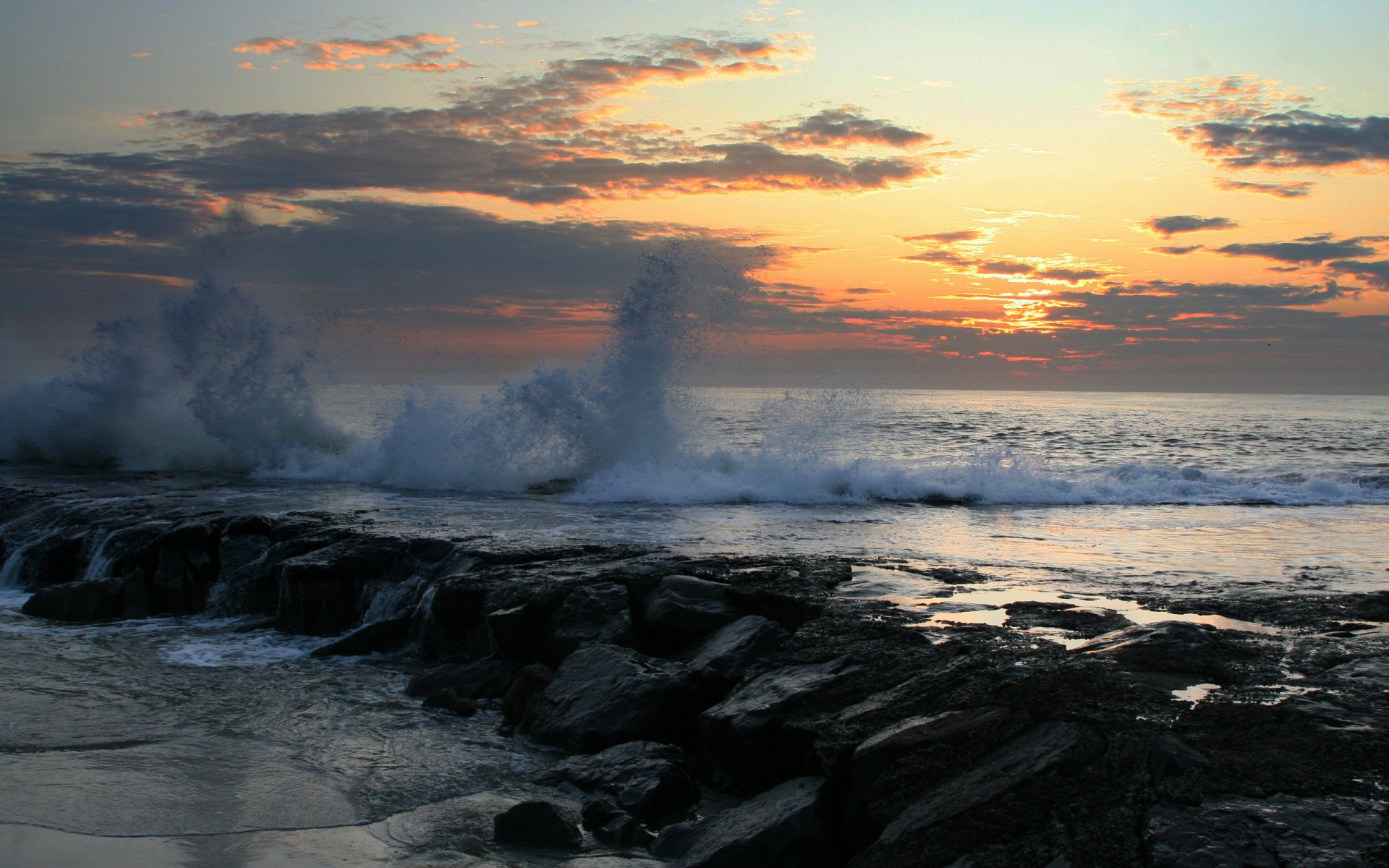 HD PC desktop wallpaper showcasing a vibrant ocean scene at sunset with waves crashing against rocky shore under a colorful sky.