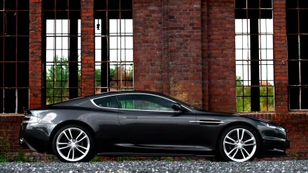 HD PC desktop wallpaper featuring a sleek black Aston Martin parked in front of large industrial-style windows and a red brick wall.