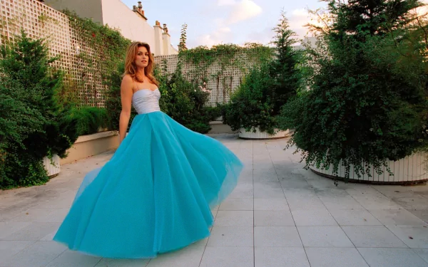 HD desktop wallpaper featuring celebrity Cindy Crawford in a flowing blue gown, posing outdoors against a backdrop of lush greenery and a tiled courtyard.