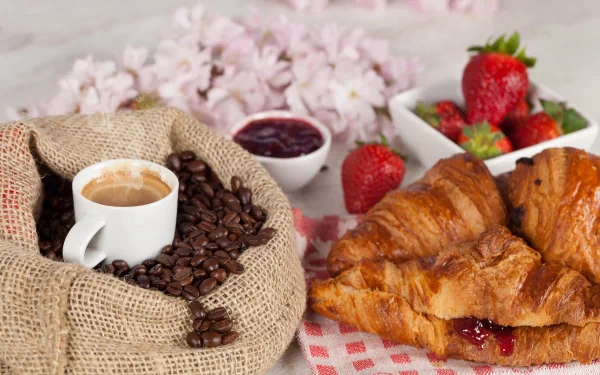 A vibrant 4K Ultra HD image featuring a cup of coffee, coffee beans, a croissant filled with jam, fresh strawberries, and delicate pink flowers on a rustic table setting.