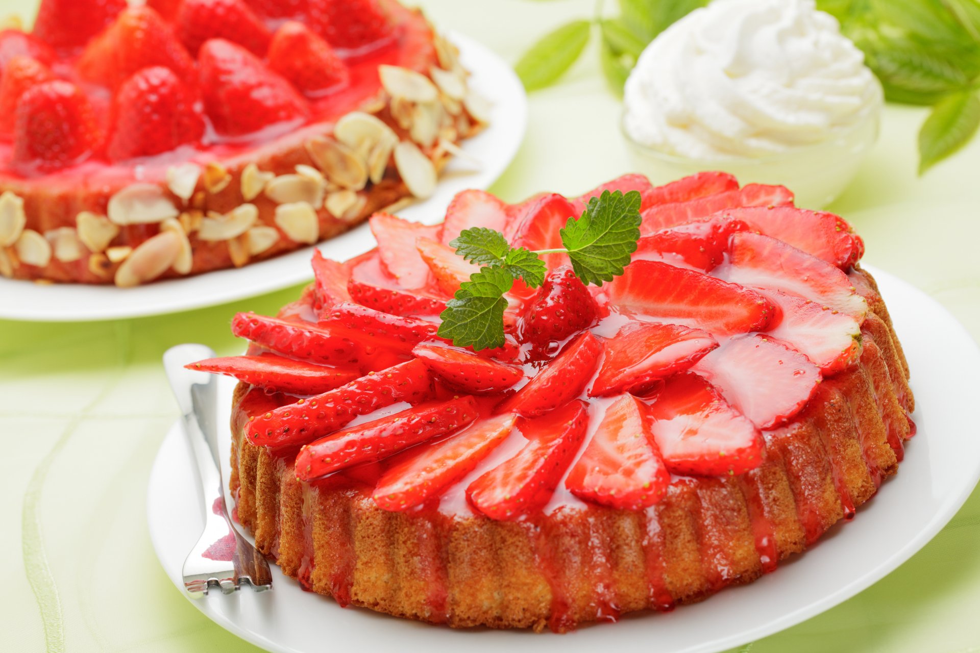 A vibrant dessert featuring a strawberry cake topped with fresh strawberries and glossy glaze, complemented by a second strawberry dessert in the background, all captured in HD quality.