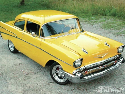 Yellow 1957 Chevrolet Belair coupe with gleaming chrome and polished wheels parked on gravel — HD PC desktop wallpaper/background.
