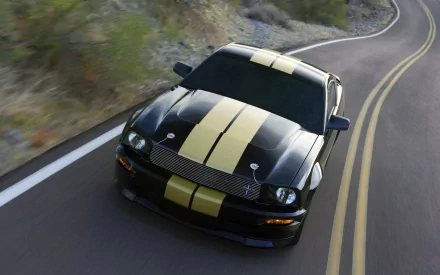 A black Ford Mustang Shelby with gold racing stripes driving on a winding mountain road, captured in high definition as a PC desktop wallpaper.