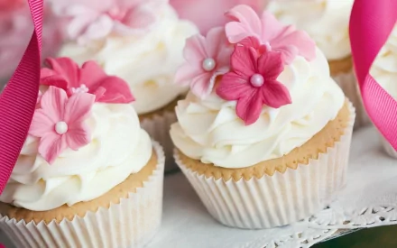A close-up of decorative cupcakes topped with white frosting and pink flower accents, set against a soft backdrop, serving as a delightful HD wallpaper for your desktop.