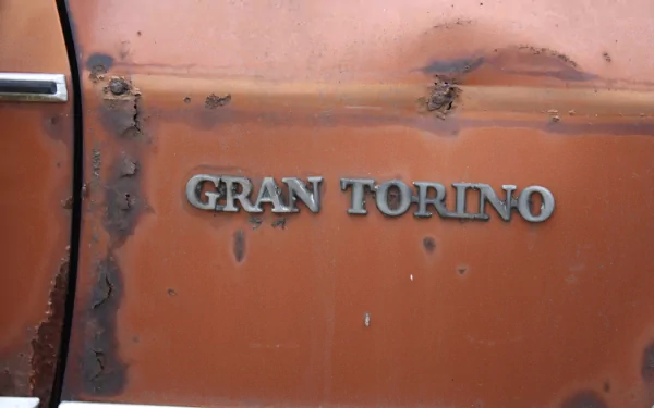 Close-up of a rusty, weathered Ford Gran Torino emblem on the orange door panel, captured in 4K Ultra HD for a PC desktop wallpaper.