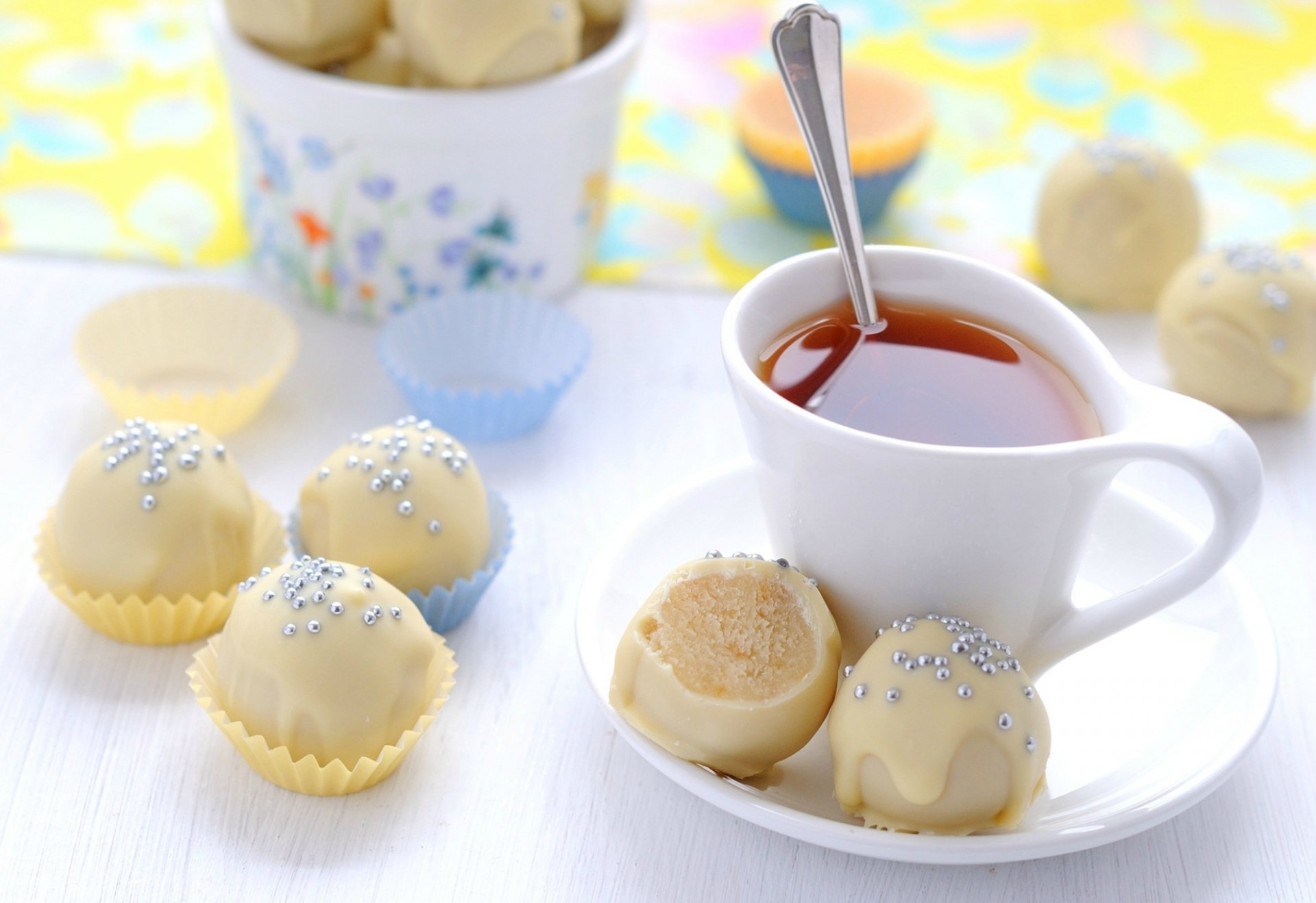 HD desktop wallpaper featuring white chocolate truffles with silver sprinkles alongside a cup of tea on a bright, softly blurred background.