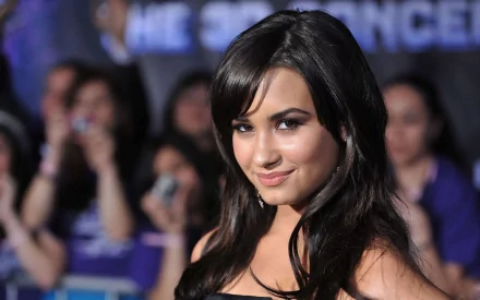 Demi Lovato poses confidently, smiling at the camera with fans visible in the background, creating a vibrant music-themed HD PC desktop wallpaper.