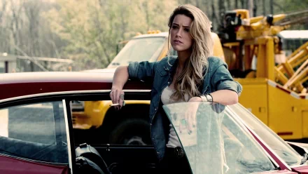 Amber Heard leans against a classic car in a scene from the movie Drive Angry, set in a gritty outdoor backdrop. This HD wallpaper captures her compelling character.