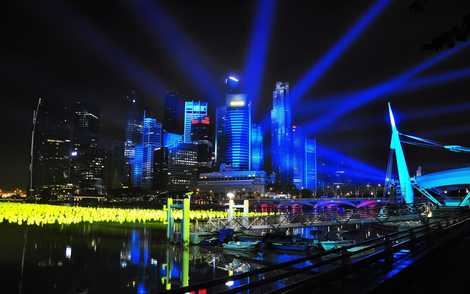 HD desktop wallpaper showcasing Singapore’s man-made skyline illuminated by vibrant blue lights and reflections on calm water at night.