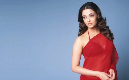 HD desktop wallpaper featuring Aishwarya Rai, the celebrity, posing elegantly in a red dress against a soft blue background.