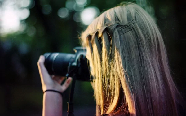 A person with long blonde hair holds a camera, capturing a scene; a 4K Ultra HD man-made PC desktop wallpaper and background image.