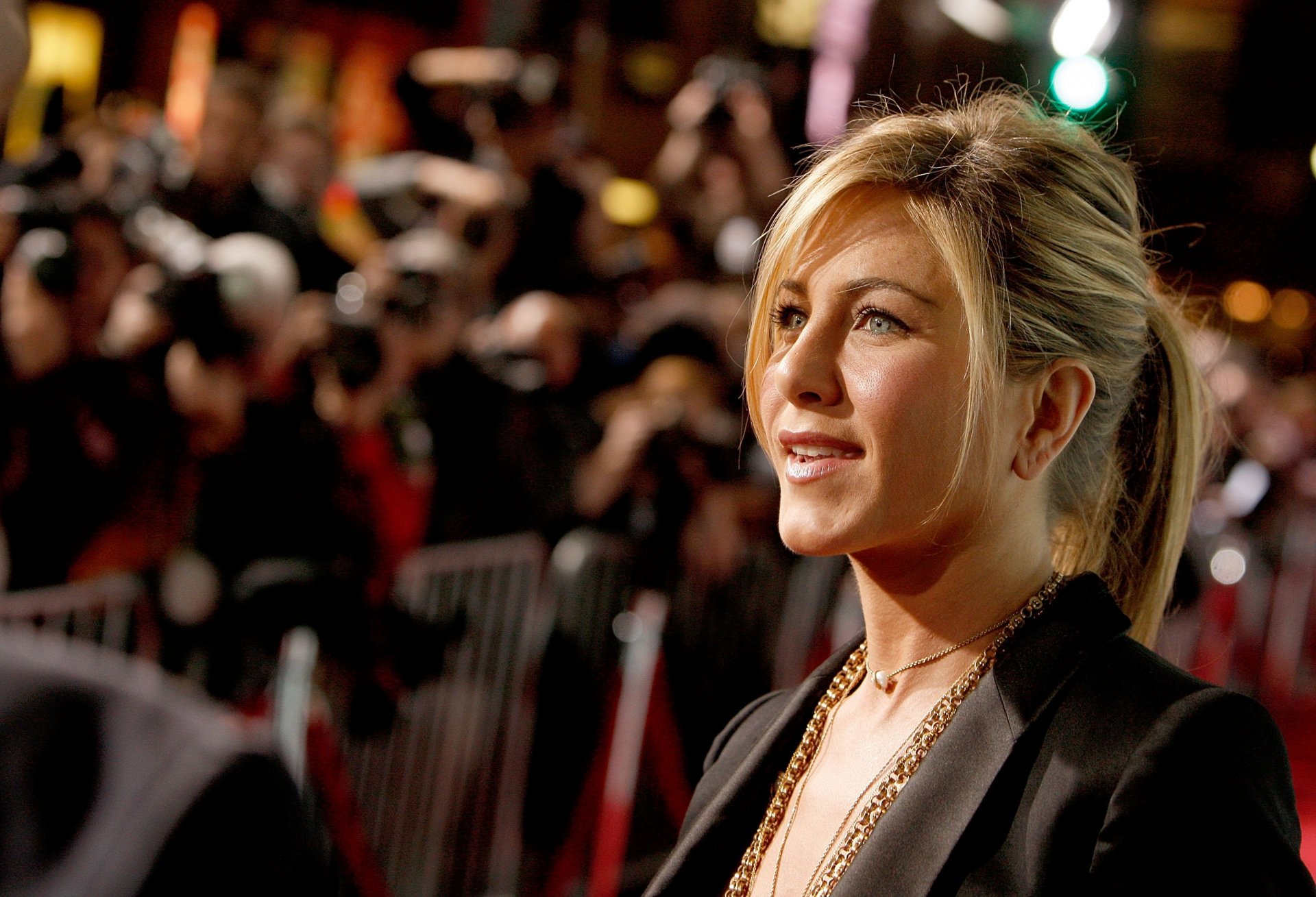 HD PC desktop wallpaper featuring celebrity Jennifer Aniston smiling against a blurred background of photographers and flashing cameras.