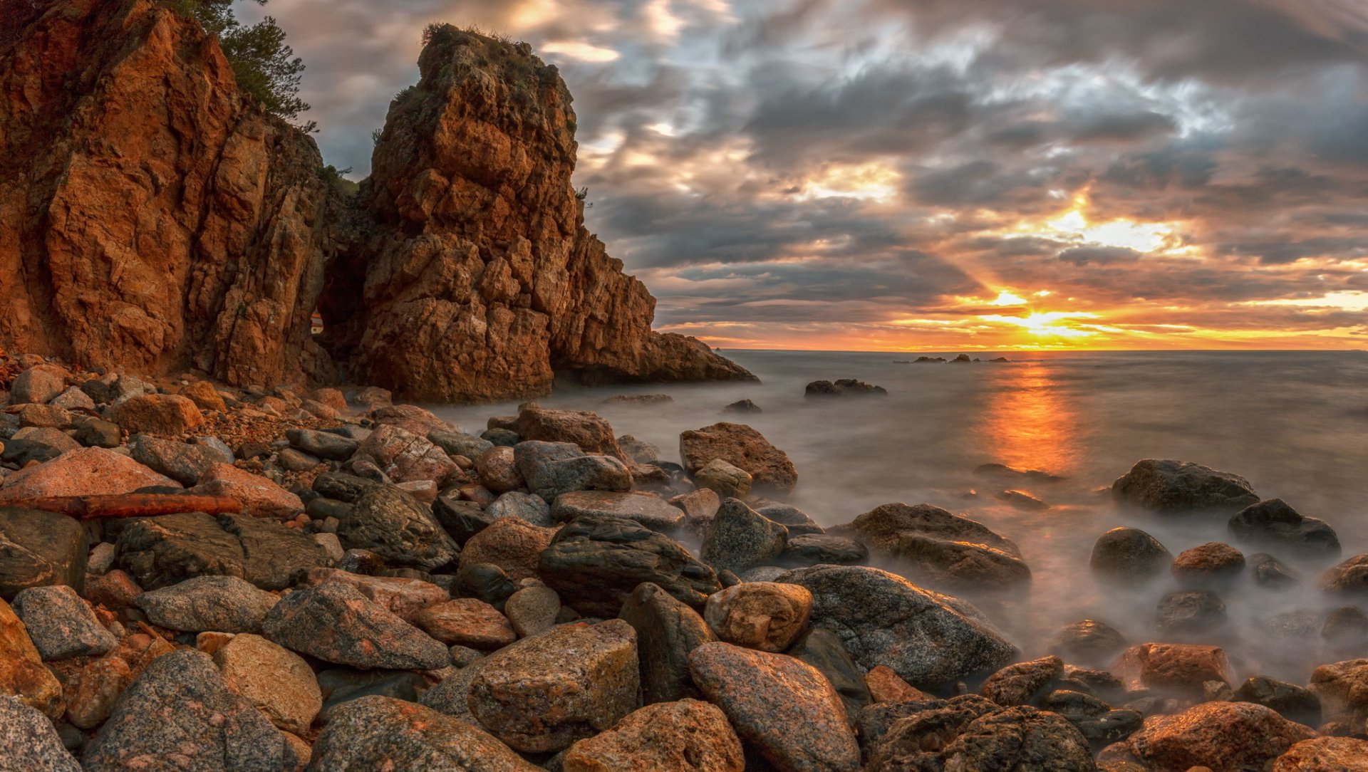 HD PC desktop wallpaper featuring a rocky coastline at sunset with dramatic clouds and soft waves, showcasing the beauty of nature.