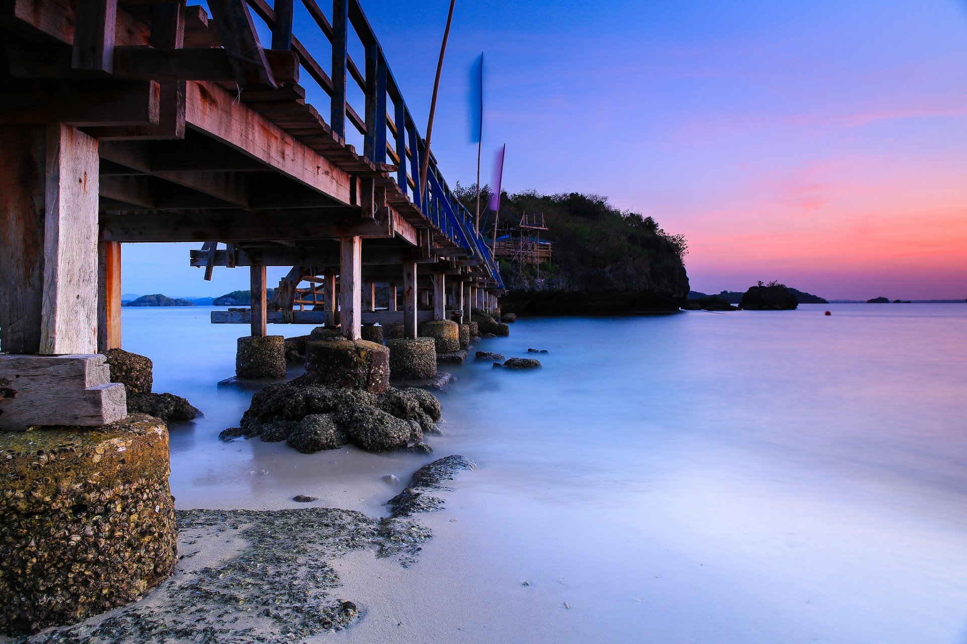HD desktop wallpaper featuring a man-made bridge extending over calm water at sunset with vibrant colors and a serene coastal landscape.