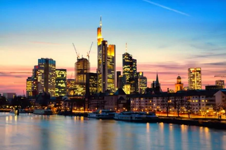 Stunning HD wallpaper showcasing the Frankfurt skyline at sunset, highlighting modern skyscrapers by the river, with vibrant colors reflecting on the water.