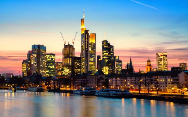 Stunning HD wallpaper showcasing the Frankfurt skyline at sunset, highlighting modern skyscrapers by the river, with vibrant colors reflecting on the water.