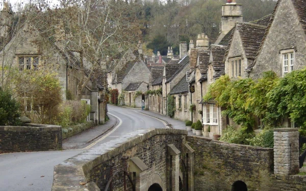 A picturesque town scene featuring charming stone houses lining a winding road, with a bridge over a small waterway, showcasing a tranquil, man-made environment.