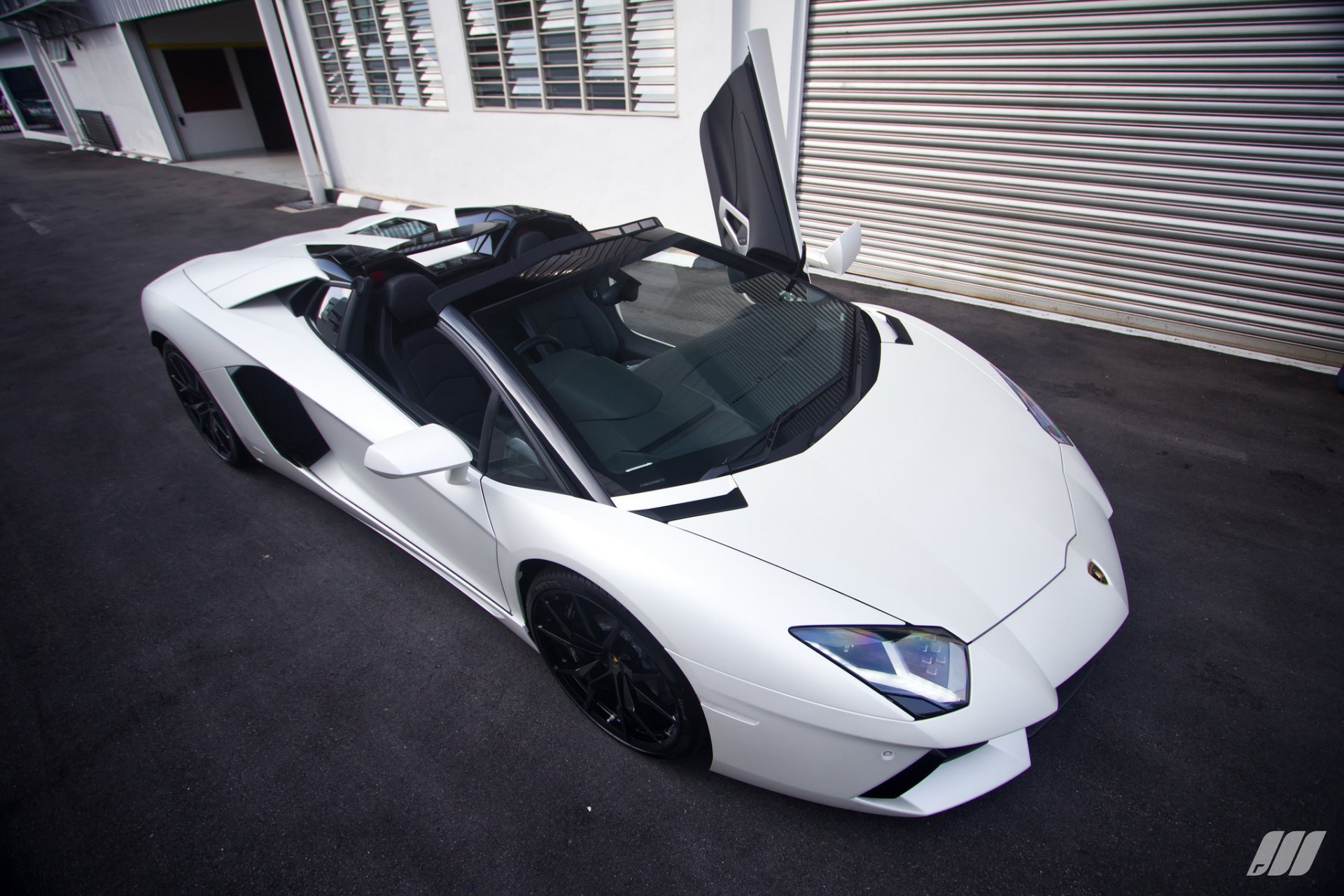 HD desktop wallpaper featuring a white Lamborghini Aventador parked on a street, with one door open, against a backdrop of buildings and a garage door.