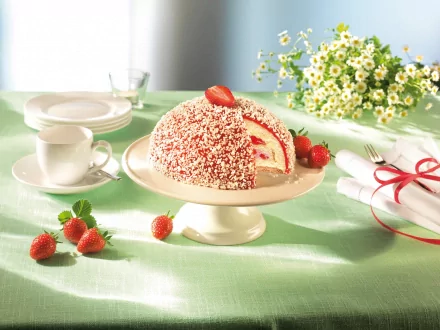 A delectable cake adorned with strawberries and chocolate sprinkles, surrounded by a chamomile bouquet, dessert plates, and a cup, set against a soft green background.
