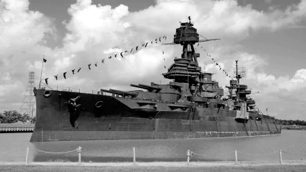Black and white HD PC desktop wallpaper featuring a large military battleship docked under a cloudy sky.