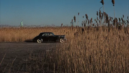 HD PC desktop wallpaper featuring a classic black car from the movie The Godfather, parked beside tall reeds with the Statue of Liberty faintly visible in the background.