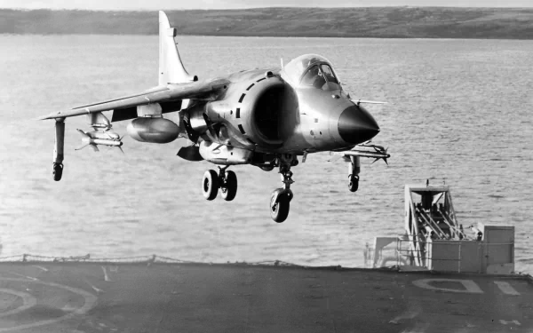 Black and white image of a McDonnell Douglas AV-8B Harrier II military jet hovering over a naval ship, captured as an HD desktop wallpaper and background.