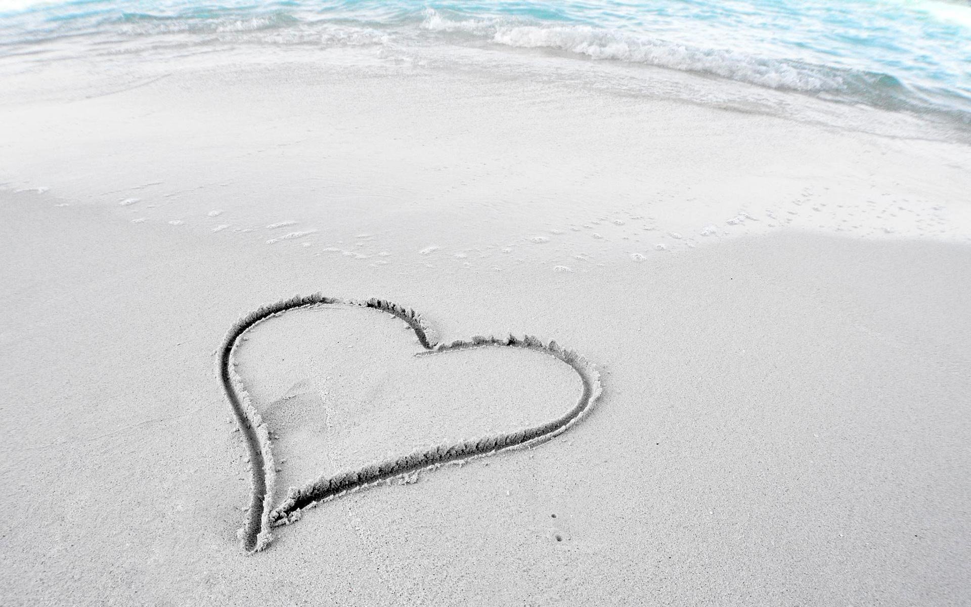 HD desktop wallpaper photography featuring a heart drawn in the sand on a beach shore, symbolizing love with gentle ocean waves in the background.