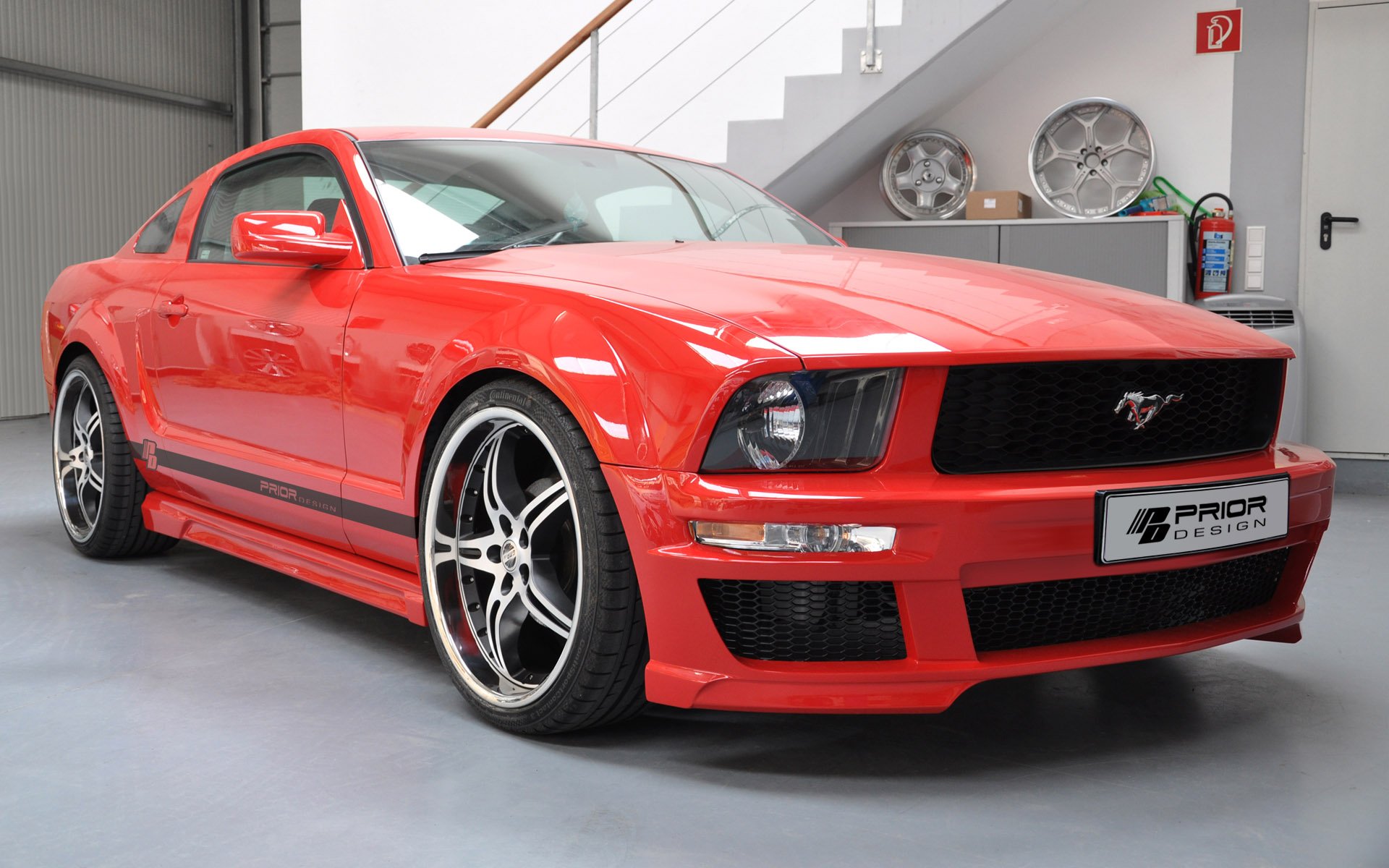 Red Ford Mustang sports vehicle in a garage, low front three-quarter view — HD PC desktop wallpaper and background.