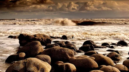 HD PC desktop wallpaper featuring a rocky shoreline with ocean waves under a dramatic cloudy sky, capturing the rugged beauty of nature.
