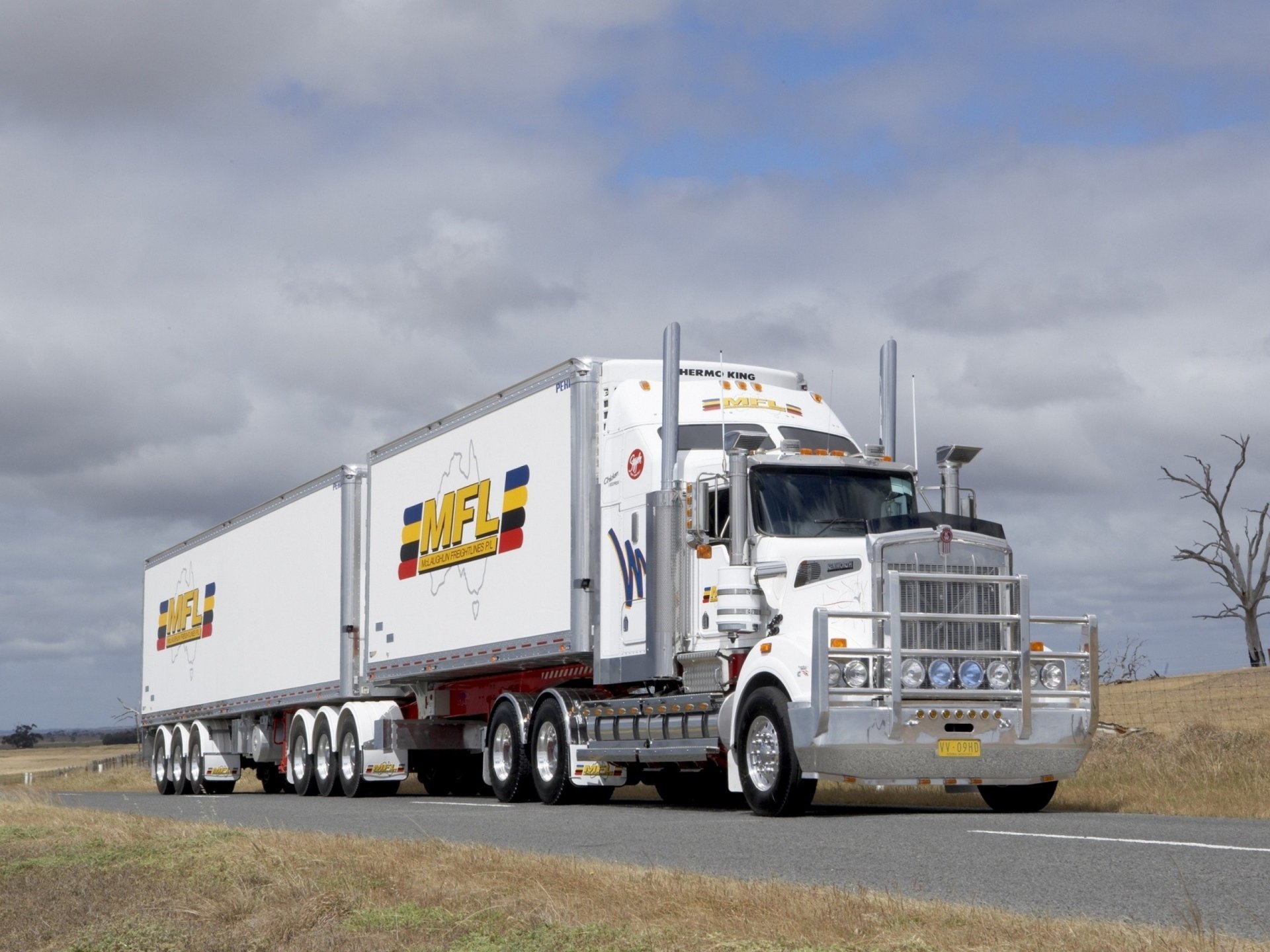 HD PC desktop wallpaper featuring a white Kenworth truck hauling dual trailers on a rural road under a cloudy sky.