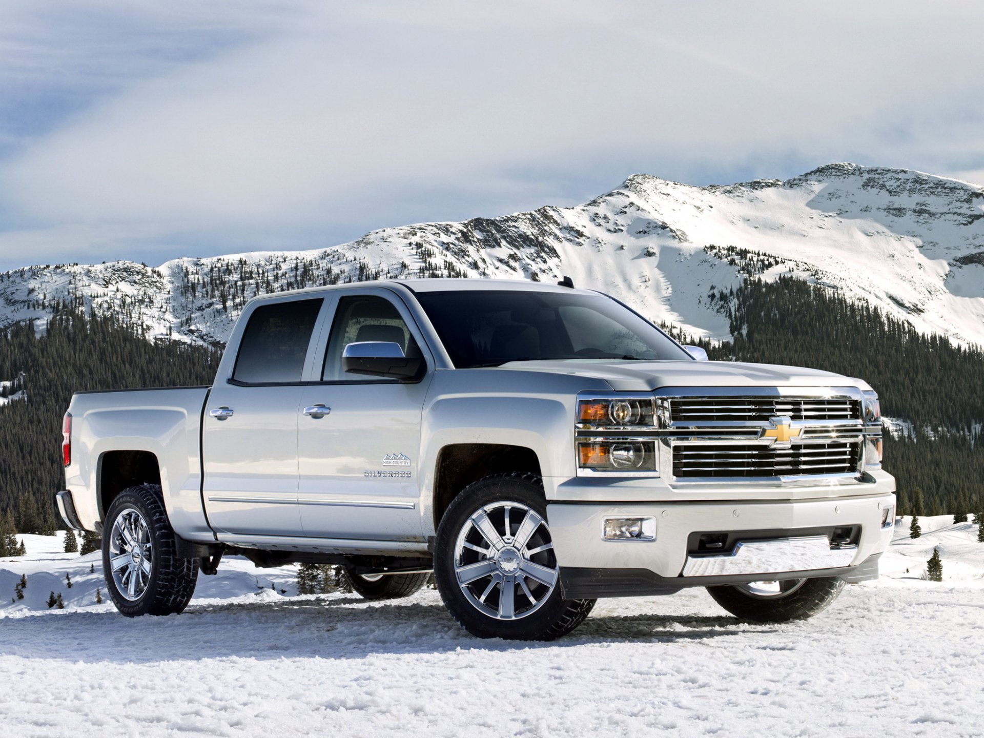 2013 Chevrolet Silverado High Country crew cab vehicle parked on a snowy mountain road, silver pickup against alpine peaks — HD desktop wallpaper.