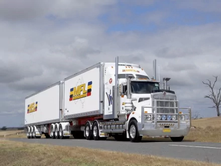 HD PC desktop wallpaper featuring a white Kenworth truck hauling dual trailers on a rural road under a cloudy sky.