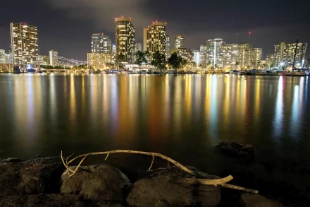 Nighttime view of Honolulu's illuminated skyline reflecting on calm water, captured in high definition for a striking man-made cityscape desktop wallpaper.