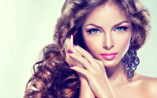 A stunning woman with flowing curls and striking makeup, elegantly posing with her hands near her face, creating an eye-catching HD desktop wallpaper.