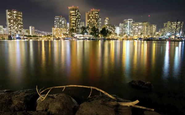 Nighttime view of Honolulu's illuminated skyline reflecting on calm water, captured in high definition for a striking man-made cityscape desktop wallpaper.
