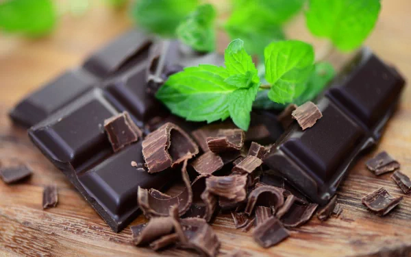 A close-up of rich chocolate pieces and curls, accented by fresh mint leaves, set against a wooden background, creating an inviting food-themed 4K Ultra HD wallpaper.