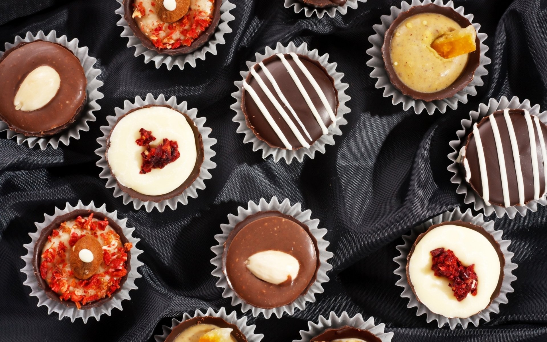 HD PC desktop wallpaper featuring an assortment of gourmet chocolates with various toppings, arranged on a dark fabric background.