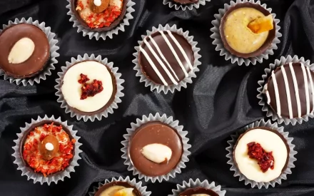 HD PC desktop wallpaper featuring an assortment of gourmet chocolates with various toppings, arranged on a dark fabric background.