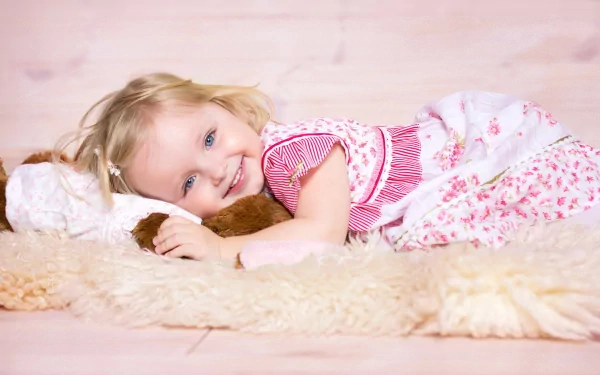 A cheerful child lies on a soft blanket, holding a stuffed animal, radiating happiness in this HD PC desktop wallpaper and background.