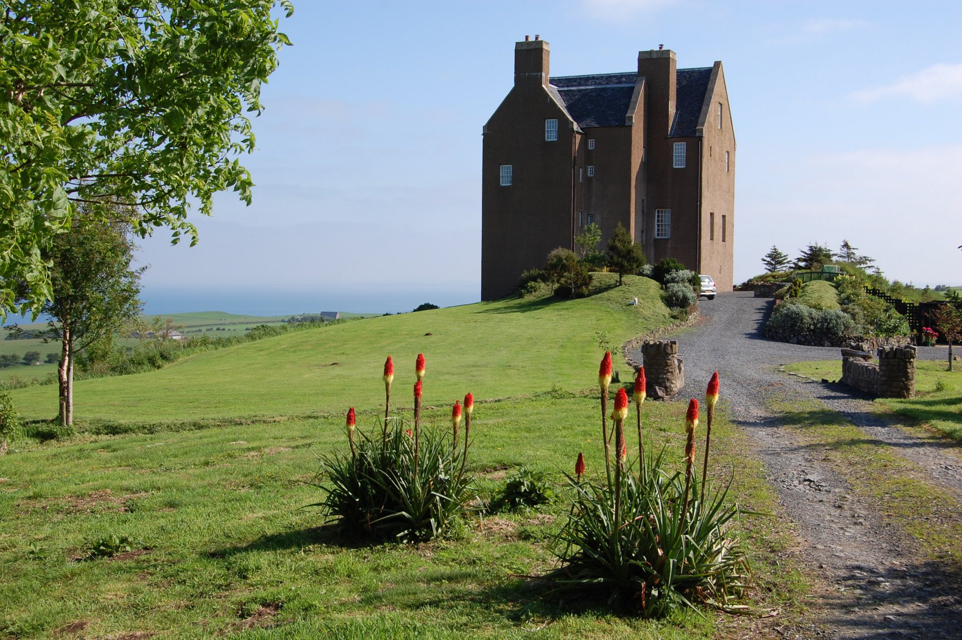 HD desktop wallpaper showcasing the man-made Dunduff Castle atop a grassy hill under a clear blue sky with surrounding greenery and a gravel path.