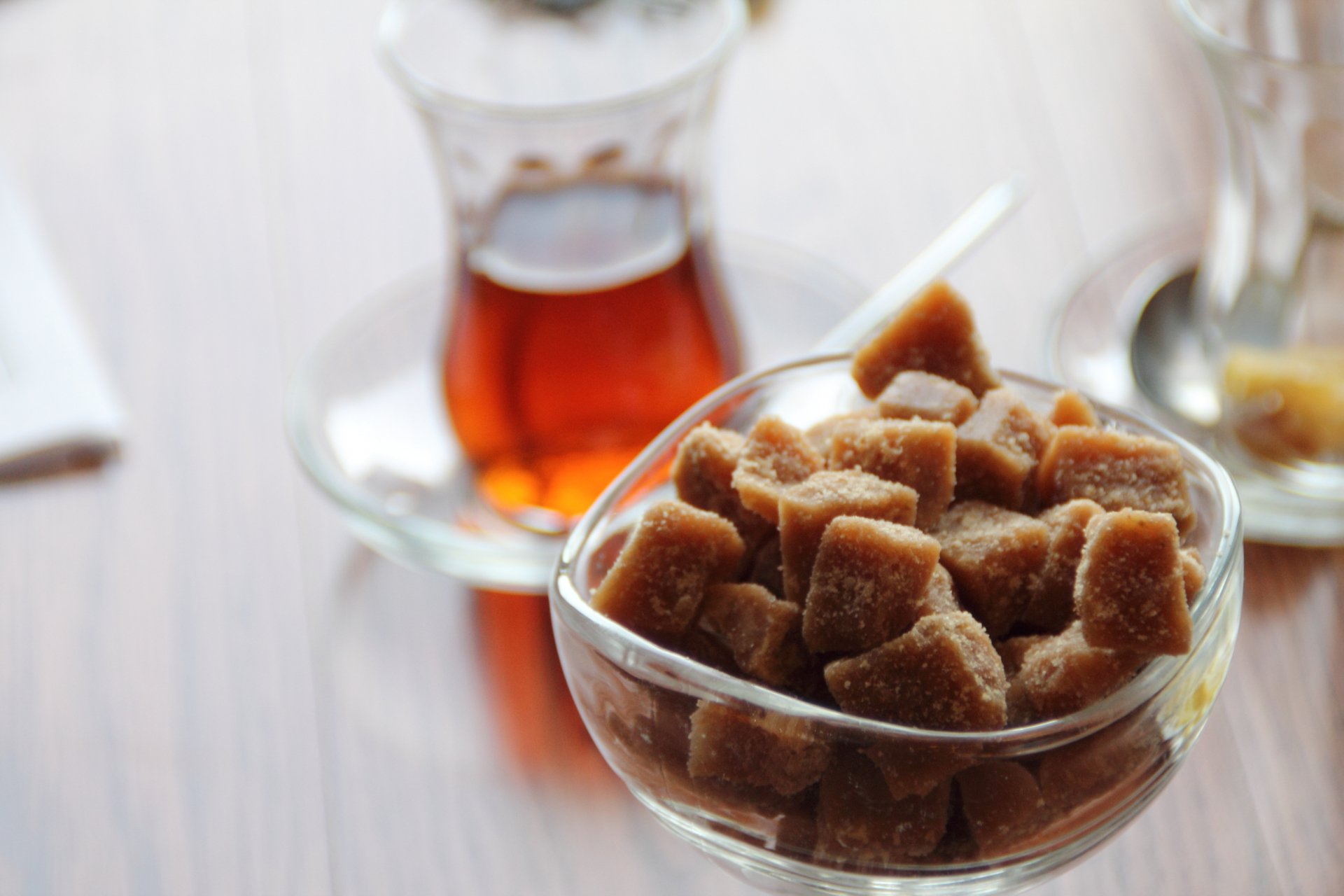 Close-up of brown sugar cubes in a glass bowl with a traditional tea glass filled with amber tea in the background, captured in vibrant 4K Ultra HD.